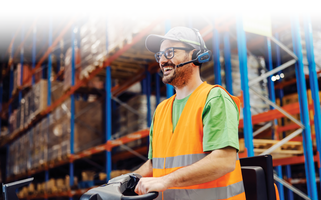 Een magazijnmedewerker bestuurt een vrachtwagen met een veiligheidshesje en headset op.