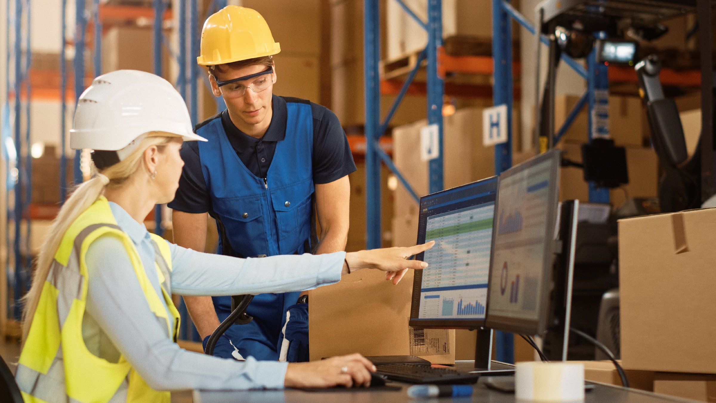 Twee magazijnmedewerkers bespreken de operaties terwijl ze ERP- en WMS-software bekijken op een scherm in een magazijn.