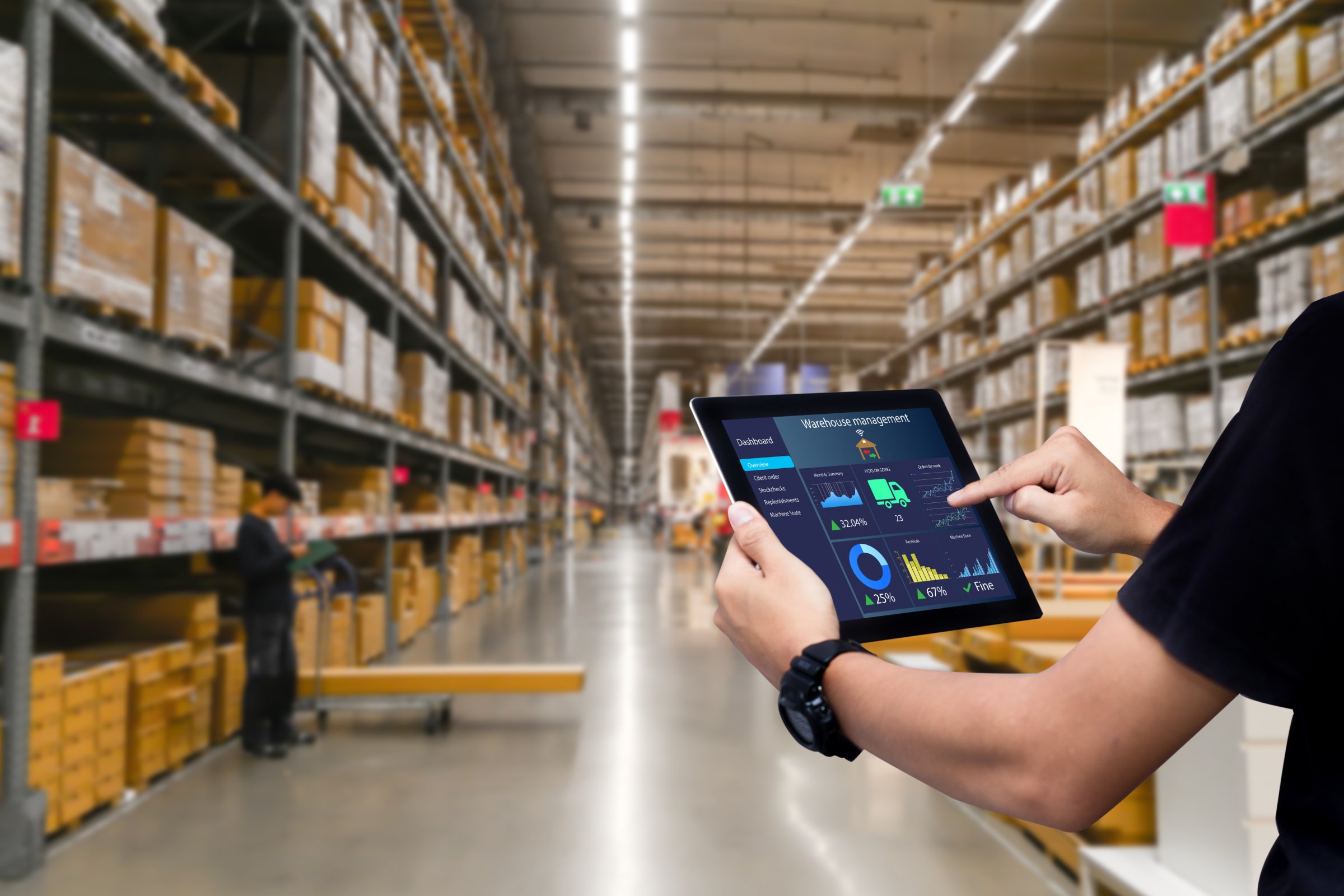 Handen die een tablet vasthouden in een magazijn met toegang tot het Warehouse Management System (WMS).